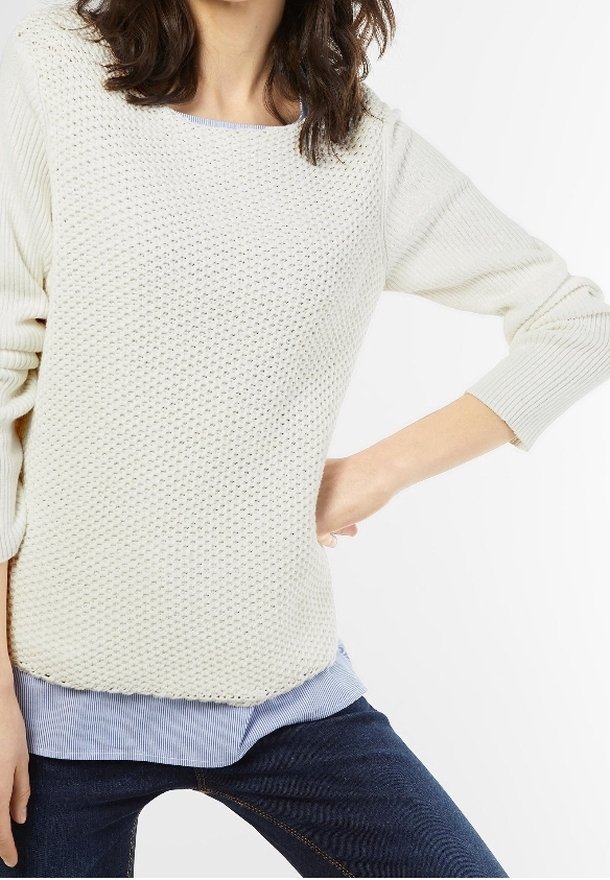 Vaalean kerma-nuori neule, jossa on teksturoitu neulekuvio, pyöreä pääntie ja kolme neljännestä hihoista, kerrostaen sinivalkoisen raidallisen paidan päällä.