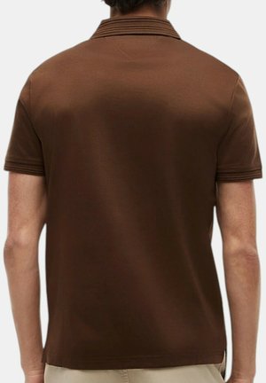 Man draagt een effen bruin poloshirt met korte mouwen, gezien van achteren, gecombineerd met lichtbeige broek.