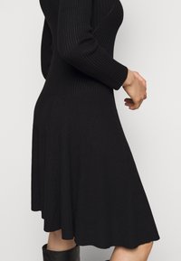 Abito nero a costine con maniche lunghe, corpo aderente e orlo svasato. Tessuto morbido con un design semplice ed elegante.