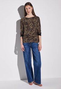 Paita pitkähihaisena leopardikuvioisena ruskean ja mustan sävyissä, yhdistettynä löysiin sinisiin farkkuihin. Ominaisuuksia ovat pyöreä pääntie ja mustat hihansuihkut.