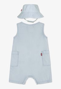 Ljusblå ärmlös overall med två fickor och en matchande spannhatt. Har ett strukturerat, mjukt tyg och en avslappnad design.