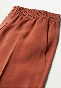 Rdzawobrązowe spodnie z elastycznym paskiem, gładką fakturą i bocznymi kieszeniami, o luźnym, swobodnym kroju.