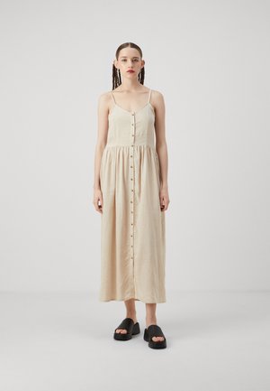 Beige linmaxikjole med tynne stropper, knappene foran og rynket midje. Sammen med svarte, kraftige åpne sko.