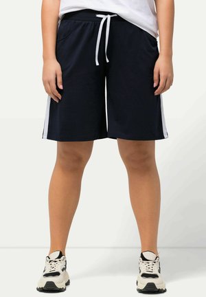 Pantalones cortos navy hechos de tela suave, con cintura elástica y cordón, bolsillos laterales y rayas blancas a los lados. Llevados con zapatillas negras y blancas.