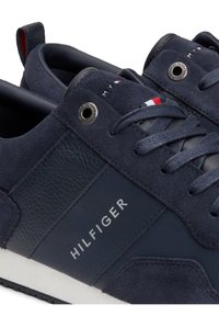 Baskets bleu marine Tommy Hilfiger avec empiècements en daim et en cuir, lacets, œillets métalliques et logo Hilfiger sur le côté.