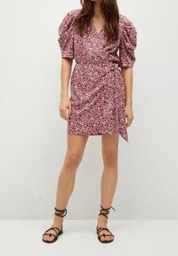Krótka kwiatowa sukienka w burgundowym kolorze z krojem w stylu wrap, z bufkami i wiązaniem w talii, zestawiona z brązowymi sandałami na paski.