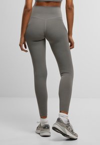 Leggings taille haute, ajustés, en un tissu gris doux, avec une texture lisse et des détails de couture subtils, associés à des baskets grises.