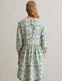 Robe florale avec des motifs verts, bleus et blancs, en tissu doux, décolleté rond, manches bouffantes trois-quarts et détail en forme de clé à l'arrière.