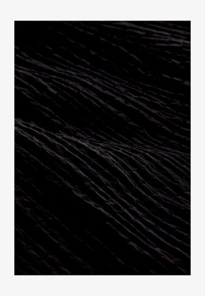 Artimas juodo audinio vaizdas su minkštais, nelygiais raukšlėmis ir klostėmis, sukuriančiomis tekstūruotą, banguotą paviršių.