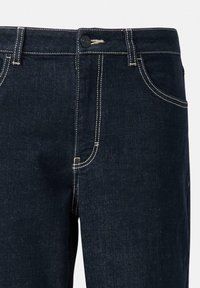 Jean en denim bleu foncé avec coutures blanches contrastantes, passants de ceinture, bouton frontal et poches visibles sur un fond uni.