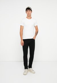 Fehér pamut póló, fekete slim-fit farmernadrág és világos színű sportcipő. A modellen szürke sapka van; jellemzője a minimalista dizájn, minta nélkül.