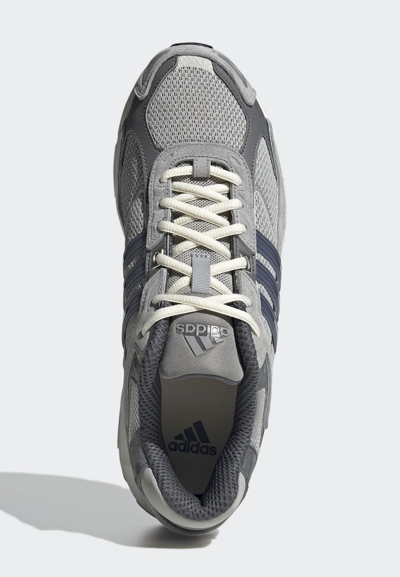Zapatilla atlética de malla gris con acentos en azul marino, que presenta cordones, una lengüeta acolchada y el logo de Adidas en la lengüeta y el lateral.