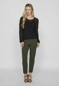 Musta pitsiga pika varrukaga topp ruudukujulise kaelusega, ühendatud kitsaste oliivroheliste pükstega ja mustade rihmadega kõrgete kontsadega, põnevate tekstuuridega.