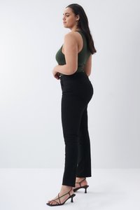 Jeans ajustados negros combinados con una blusa sin mangas de color verde oscuro. Incluye un diseño de cintura alta, textura suave y diseño minimalista. Tacones negros con tiras.