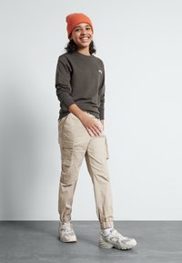 Mørk grå hettegenser med mansjetter, oransje lue, beige cargo-bukser med lommer og grå joggesko. Glatte teksturer, uformell passform.