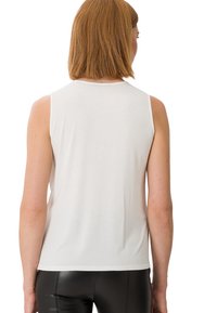 Haut blanc sans manches avec une texture lisse, décolleté rond, et coupe décontractée, associé à un legging noir brillant et ajusté.