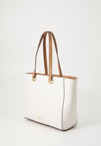 Sac fourre-tout blanc avec quincaillerie dorée, poignées en cuir marron et un design structuré. Il présente une texture lisse et des détails de bord contrastants en couleur foncée.