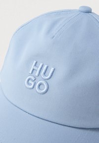 Ανοιχτό μπλε καπέλο του μπέιζμπολ με ριμπ όψη και κεντημένο λογότυπο "HU GO" στο μπροστινό μέρος. Διαθέτει στρογγυλεμένο στέμμα και γείσο.