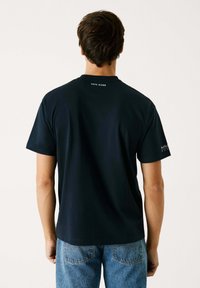 Camiseta de algodón azul marino de manga corta, con cuello redondo y logo en la parte posterior del hombro; combinada con jeans de mezclilla azul claro.