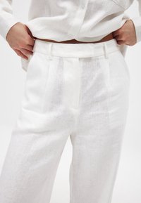 Balti lina bikses ar br�īvu piegriezumu, ar miegainu priekšpusi un sānu kabatām. Gluda tekstūra ar smalku auduma rakstu.