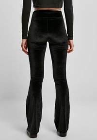 Mustat samettiset liehuvat housut, joissa on korkea vyötärö, sileä pinta ja hienovarainen kiilto, suunniteltu istuvaan siluettiin ja levenevään lahkeeseen.