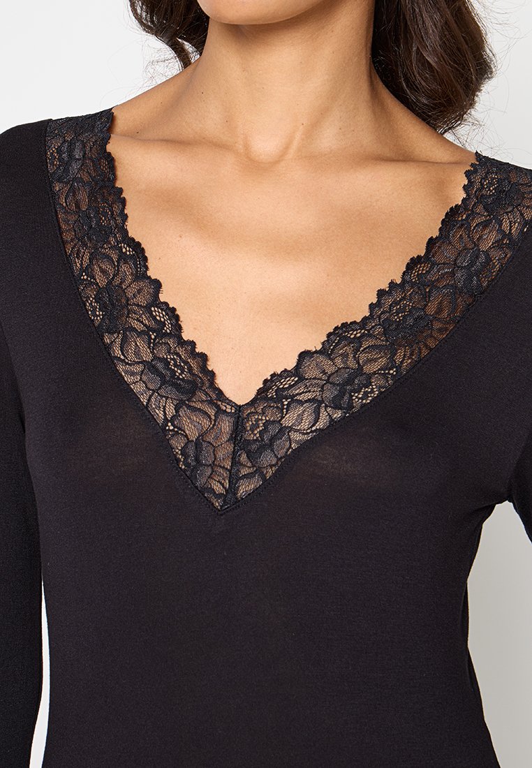 Top nero con scollatura a V profonda, rifinito con delicata pizzo nero che mette in evidenza motivi floreali. Tessuto morbido con un design aderente.