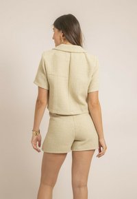 Veste cropped à manches courtes et shorts assortis en tissu beige texturé avec un motif tissé. Présente un col droit et une poche au dos.