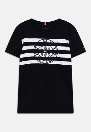 T-shirt noir à manches courtes avec des rayures blanches horizontales et un logo circulaire "Tommy Hilfiger 1985" avec une boussole au centre.