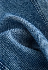 Sinine denim kangas pehme ja tekstuuriga pinnaga, millel on peened õmblused ja õrn volt.