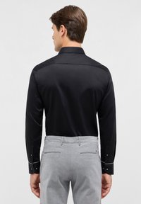 Zwarte lange mouwen shirt met een gladde textuur, gestructureerde kraag en contrasterende witte stiksels op de manchetten, gedragen met lichtgrijze broek.
