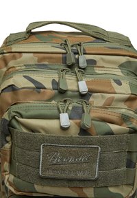 Kamuflāžas mugursoma, kas izgatavota no izturīga auduma. Piedāvā trīs rāvējslēdzējus ar pelēkiem vilkšanas cilpiņām un uzlīmi ar "Brandit" zīmolu. Zaļās akcenti.