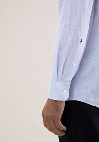 Camicia azzurro chiaro con motivo a fantasia, tessuto lavorato, polsini bianchi con bottoni e dettaglio nero sulla manica. Design aderente.