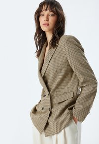 Blazer doppiopetto in un motivo a quadri marrone e beige, con vestibilità sagomata, rever a punta e tasche laterali. Tessuto morbido.