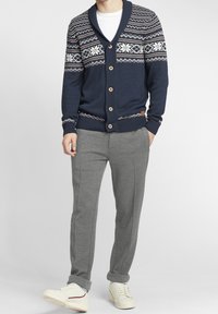 Cardigan bleu marine avec motifs flocons de neige et fermeture à boutons, associé à un pantalon de survêtement gris et des baskets blanches. Tricot texturé avec poignets côtelés.