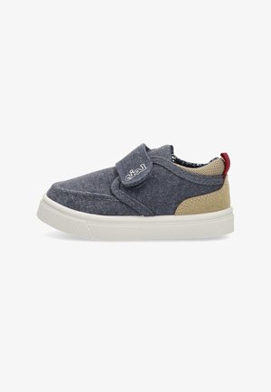 Zapato slip-on de denim en azul oscuro con acentos beige, correa de Velcro, suela texturizada y forro interior estampado.