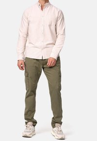 Lys beige knap-inder skjorte med en lomme, parret med olivengrønne cargo-bukser med sidelommer og lyse atletik sko.