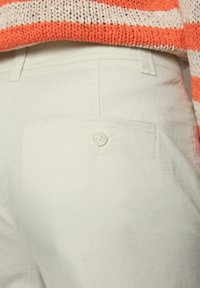 Ljust färgade byxor har en liten ficka på höger bak med vit knappstängning, i kombination med en randig tröja i orange och krämfärgad.
