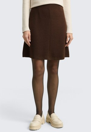 Jupe A-line marron en tissu texturé, avec un design mi-long. Associée à des mocassins à plateforme de couleur crème et des collants noirs.