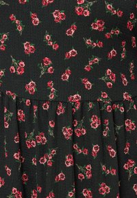 Svart tyg med ett litet blommönster av röda rosor med gröna blad, texturerad yta och en rynkad volangdetalj längs fållen.