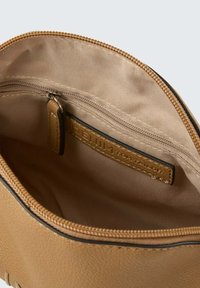 Binnenkant van een tan faux leren tas, met een gladde, gevoerde afwerking, een ritsvak en een label. Rits- en stiksels zijn zichtbaar.