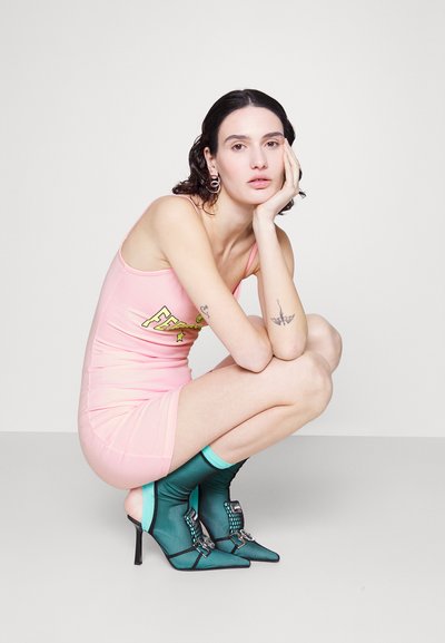 Ροζ αμάνικο φόρεμα με γραφικό σχέδιο, συνδυασμένο με τιρκουάζ μποτάκια μέχρι τον αστράγαλο με μυτερή μύτη και διακοσμητικές λεπτομέρειες.