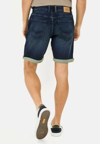 Shorts en denim bleu foncé avec des ourlets retroussés, cinq poches et un patch en cuir au dos. Associés à des chaussures blanches et bleu marine.