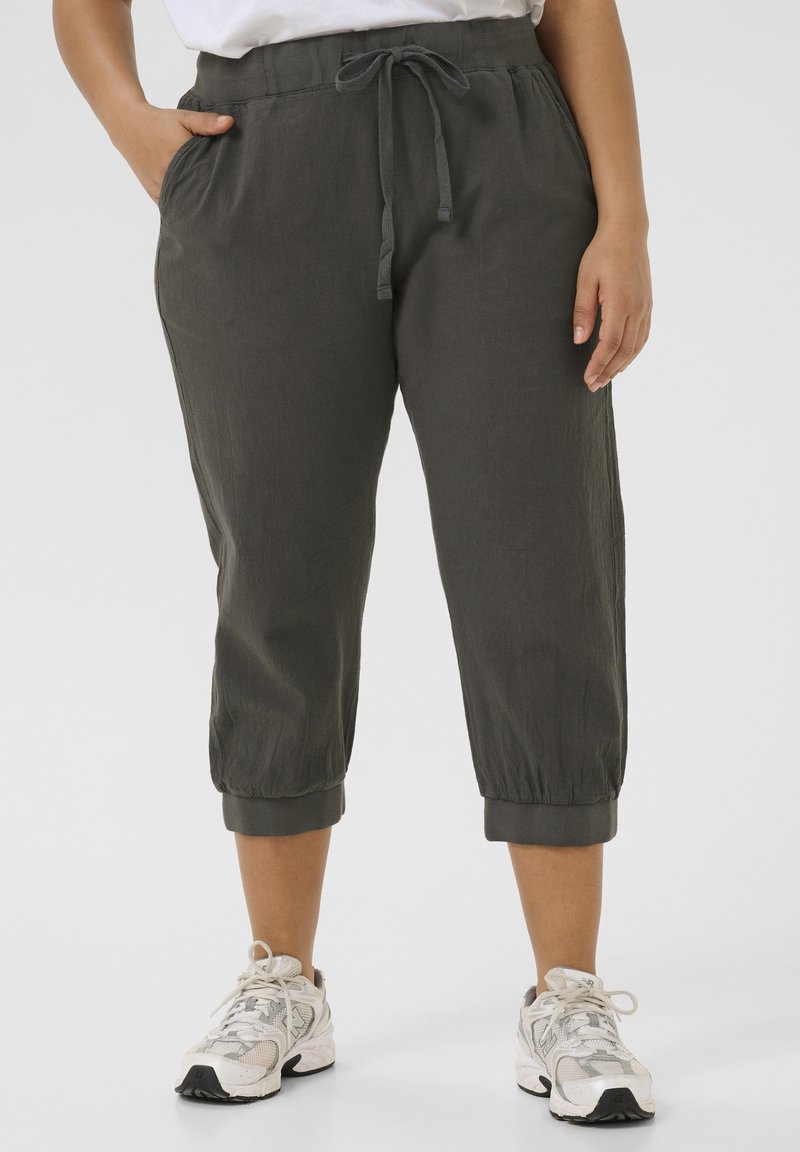 Pantaloni corti grigio scuro con elastico in vita e stringa, dotati di tasche laterali e polsini aderenti. Indossati con sneakers di colore chiaro.