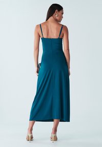 Teal satiinimidi mekko ohuilla olkaimilla, istuvalla yläosalla ja sivusiteillä. Varustettu vetoketjulla ja hellävaraisella drapeerauksella, joka parantaa liikettä.