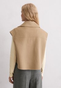 Beige mouwloze vest met kraag, gemaakt van zachte stof, met een nette, gestructureerde achterkant en een middenlange lengte, gecombineerd met een beige top.