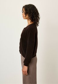 Brown, soft knit cardigan with a relaxed fit, round neckline, and dropped shoulders, worn over a gray, mid-length skirt.
