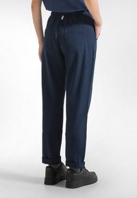 Marineblauwe, lichte katoenen broek met elastische tailleband, toelopende pijpen en omgeslagen manchetten. Beschikt over twee achterzakken.