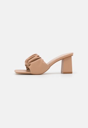 Beige mule med åben tå, rynket strop og blokhæl, vist i sideprofil på en ensfarvet lys baggrund.