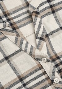 Ein kariertes Hemd in einer Mischung aus Beige, Schwarz und Grau, mit einer sanften Textur, Knopfdetails und einem Kragendesign.