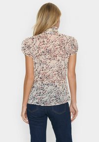 Floral-patterned blouse in lightweight, sheer fabric. Features puffed short sleeves, high neckline, and colors in red, blue, and beige.